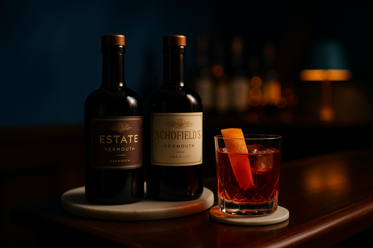 Two bottles of Asterley Bros vermouth, ESTATE and SCHOFIELD'S, beside a glass of Negroni